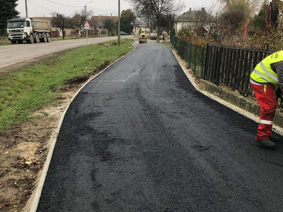 Járda aszfaltozása lakóövezeti utcában – hengerlés folyamatban, szegélykő mellett
